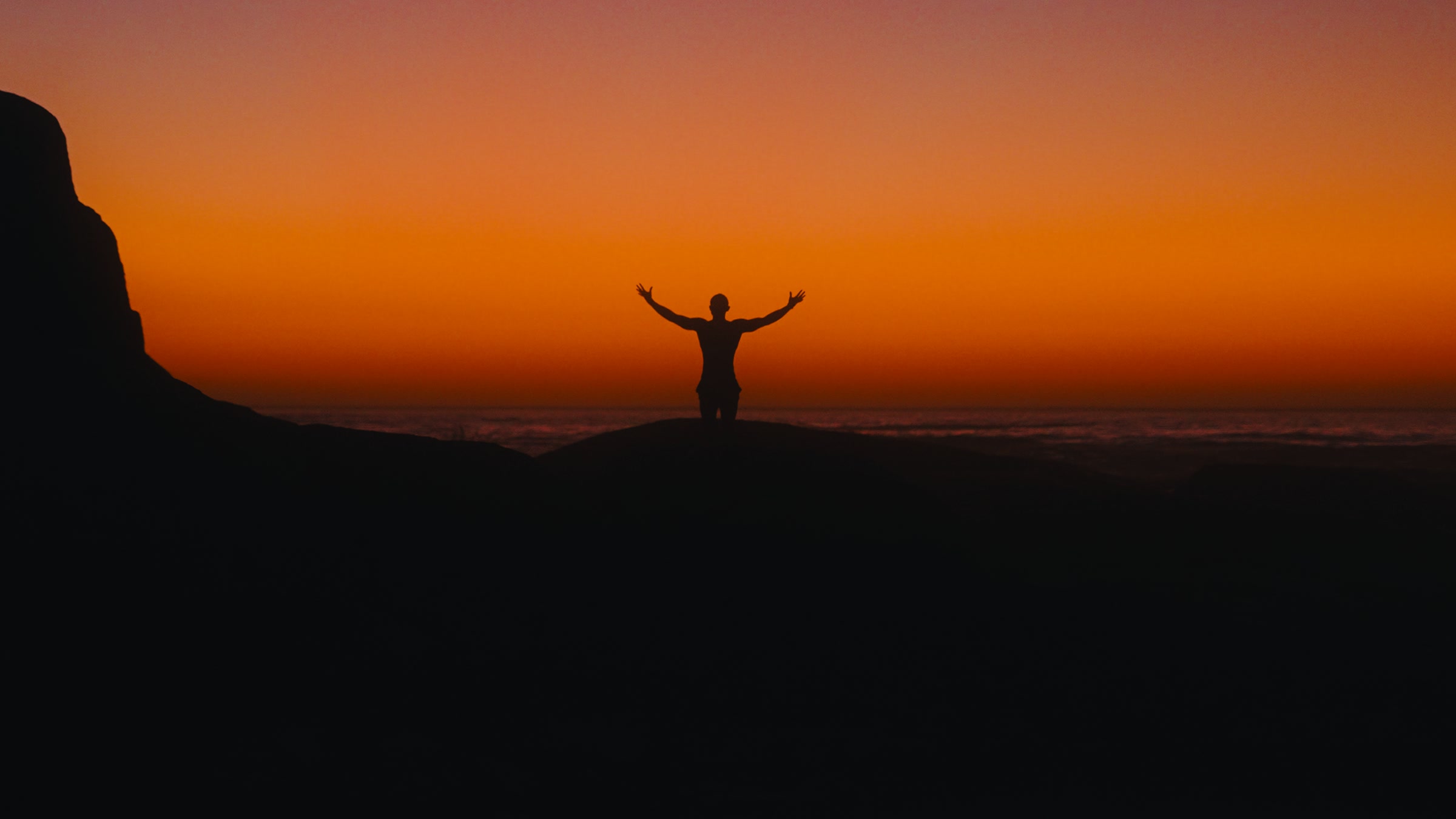 Graded frame: a figure with arms raised against a deep orange sunset